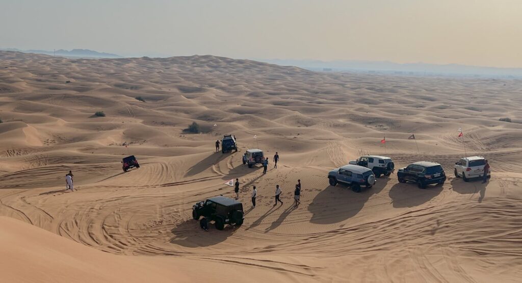 A group of SUVs and people explore the sand dunes in Sharjah, UAE.