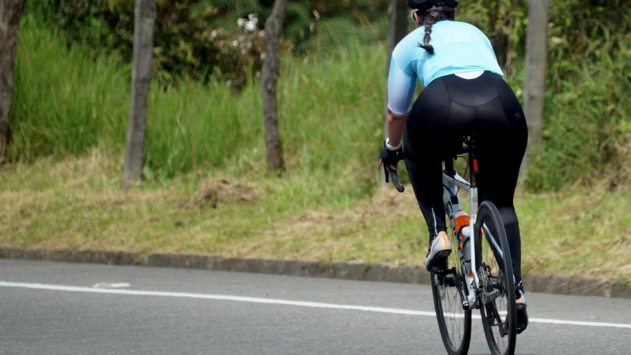 Rear view of a woman cycling on a tranquil, open road surrounded by nature.