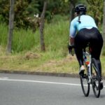 Rear view of a woman cycling on a tranquil, open road surrounded by nature.