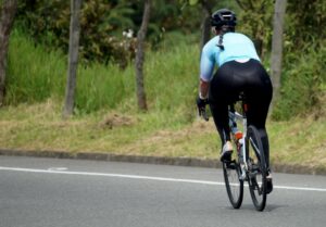 Rear view of a woman cycling on a tranquil, open road surrounded by nature.