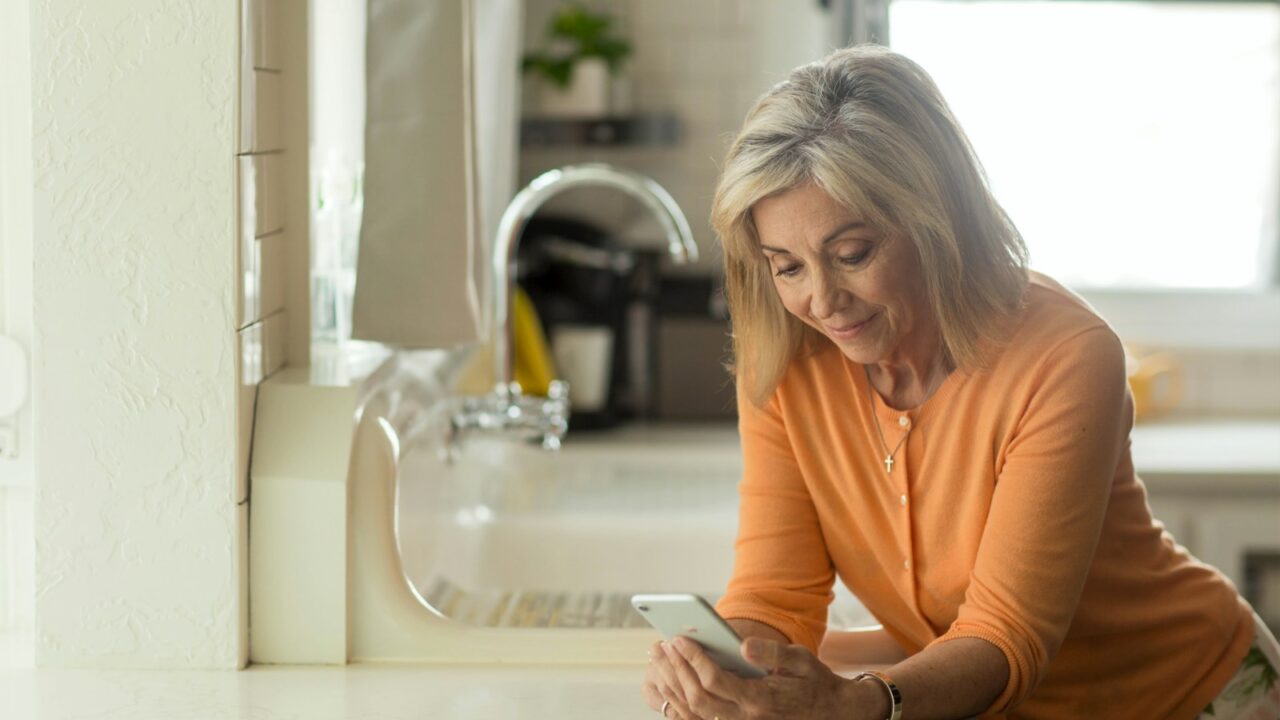 woman in orange long sleeve shirt using white smartphone